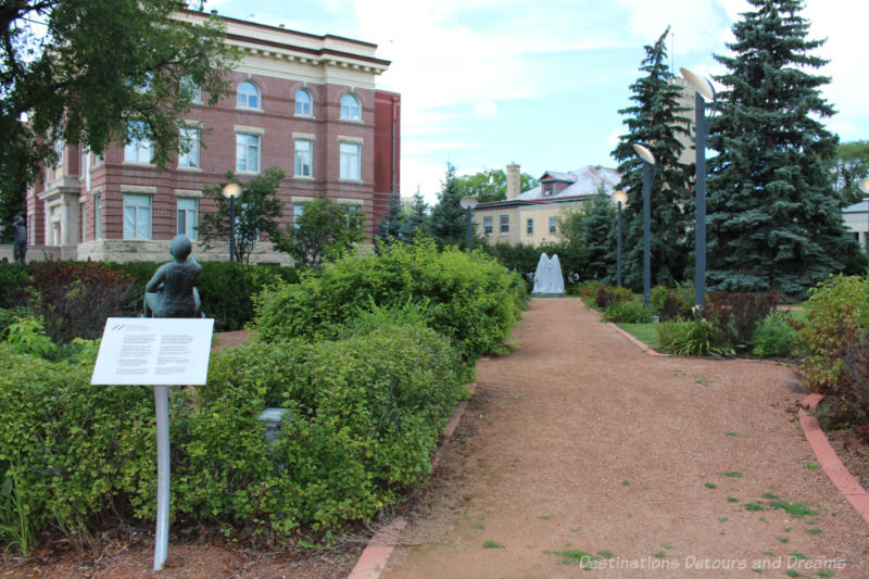 Path into a landscaped sculpture garden beside an early 1900s red brick building in Saint Boniface, Winnipeg