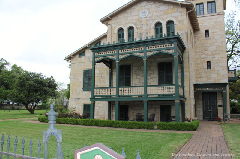 Three story brick heritage home with green trim verandas in San Antonio King William district