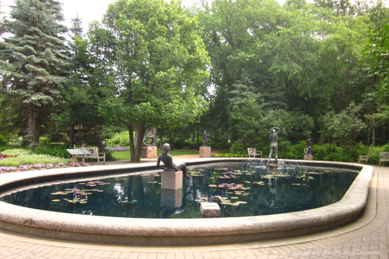 Fountain with a couple of sculptures in in surrounded by trees and garden area