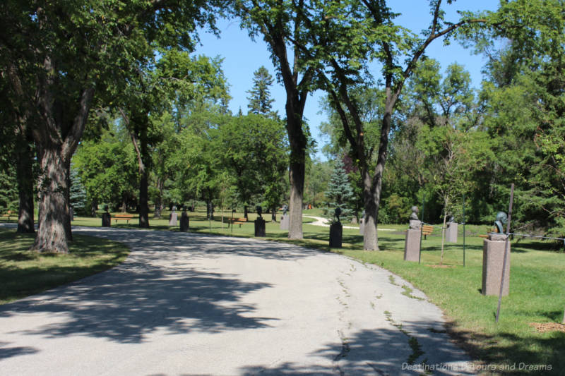 Walkway in park bordered by trees featuring busts of citizens on pedestals along the walkway