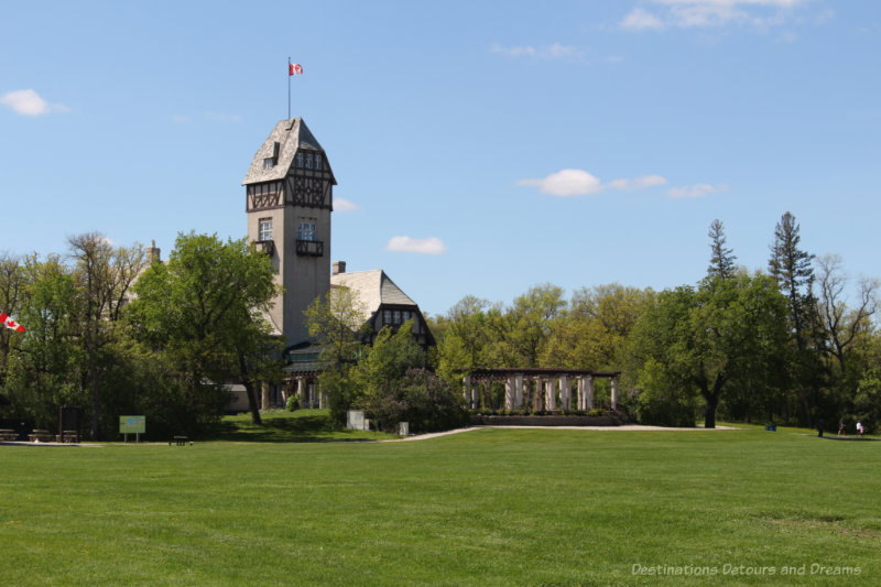 Tower of Pavilion building flanked by trees at the back of a green lawn area in Assiniboine Park