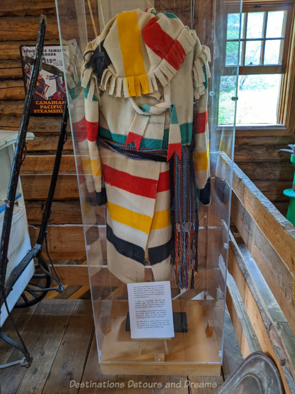 White, red, yellow, and green striped handmade wrap-type coat (capote) with fringe hood on display in mill museum