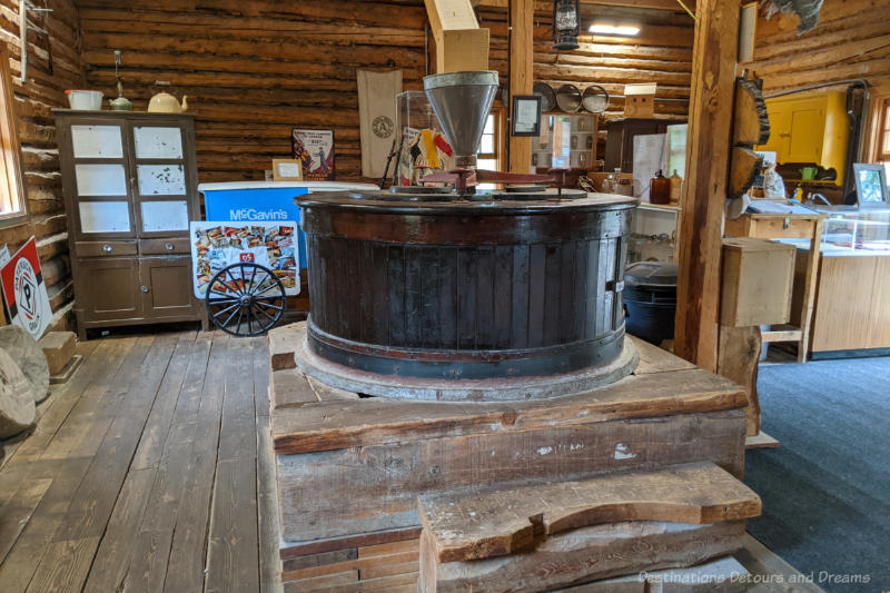 Inside of a water mill replica with wood walls and floors and huge grindstone in centre