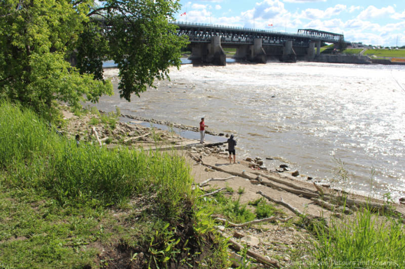 Two people fishing on river by bridge with lock and dam