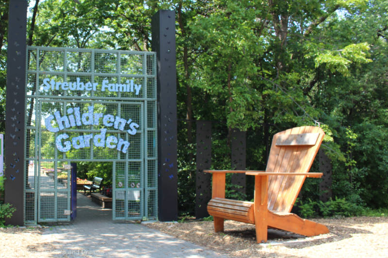 Large Muskoka chair beside wire screen door entrance to a Children's Garden