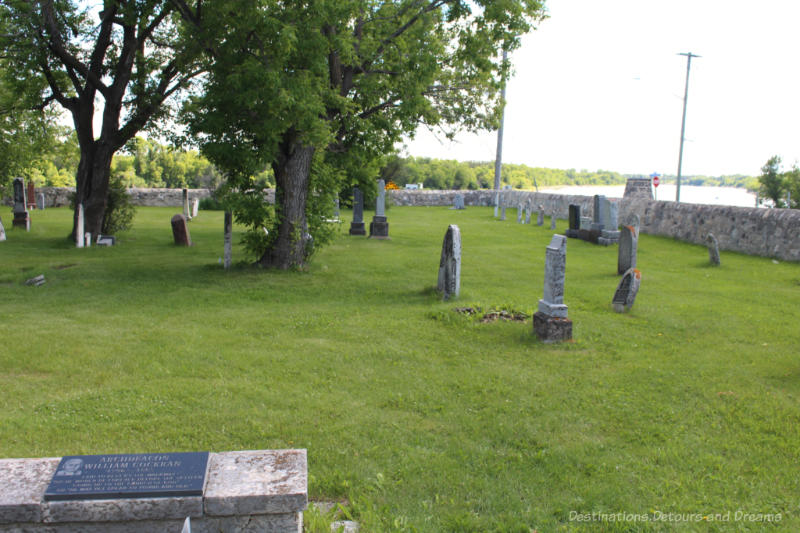 Cemetery of old tombstones inside a stone fenced area with a view of the river in the background