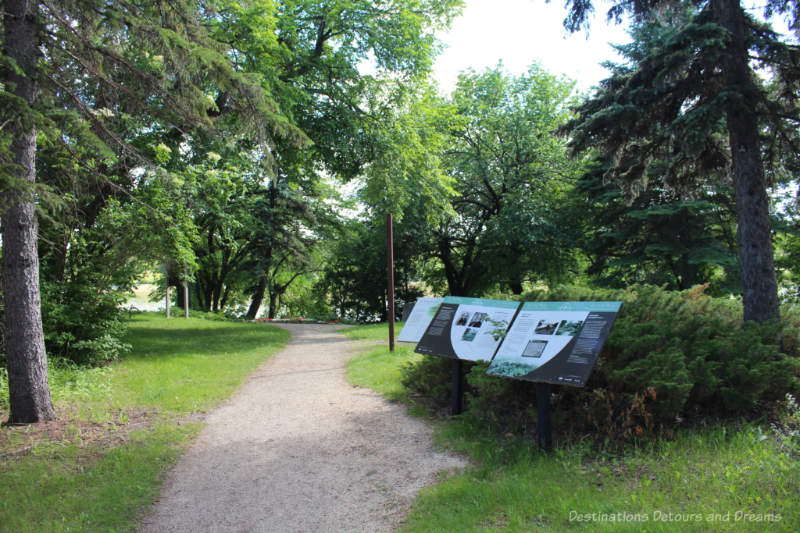 Path through green wooded area to a garden with interpretive signs along the side of the path