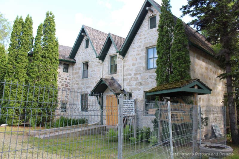 A two-storey historic stone house behind wire fencing as it is being restored