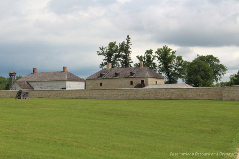 Stone and wooded buildings of a fur-trading fort inside a stone fence