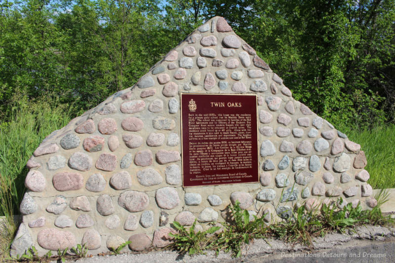 Stone marker alongside road with a plaque on it commemorating a former school on the site