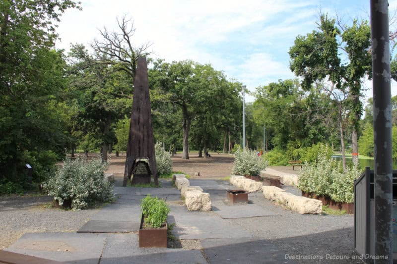 plaza area in park featuring stone seating, art structure fireplace, and surrounding trees