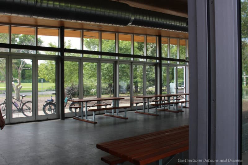 Picnic tables inside a park pavilion with a full windowed wall with view into park