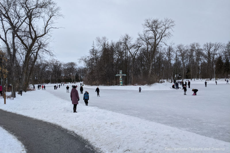 People skating on a frozen park pond with bare deciduous trees bordering the pond