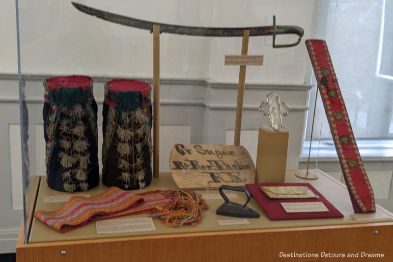 Collection of items including beaded moccasins and Métis sash, inside museum display case