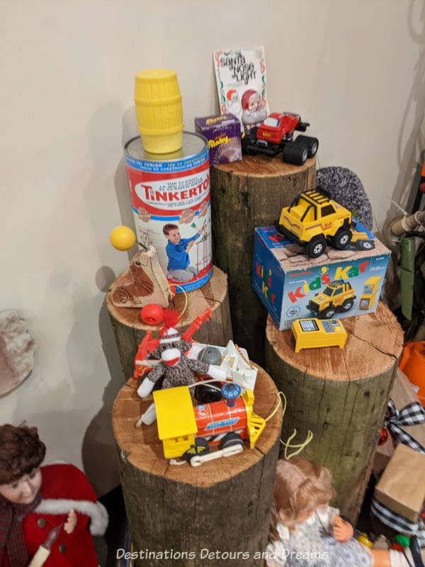 A collection of old toys (Tinkertoys, Slinky, truck, doll, etc.) display on and beside tree stumps