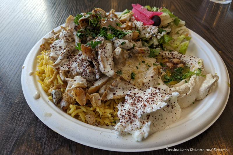 Plate of chicken shawarma on rice with Greek salad, hummus, and garlic sauce