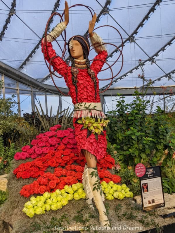 Floral display in honour of Folklorama features mannequin in dress of red blooms doing Indigenous hoop dance