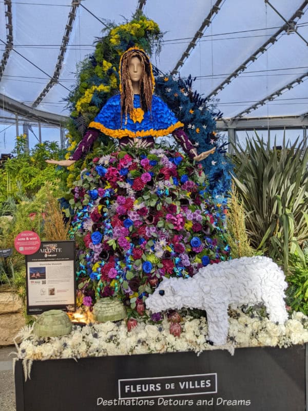 Mannequin wearing bright floral dress with floral polar bear at her feet in a floral art show