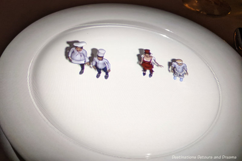 Animated projection of four tiny chefs onto a white dinner plate