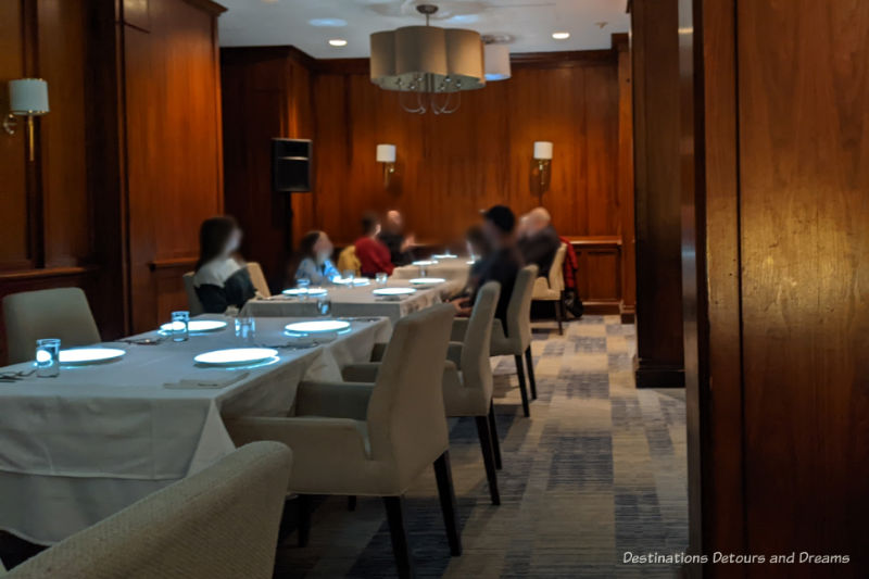 Wood-paneled restaurant with tables covered in white table clothes and white upholstered chairs